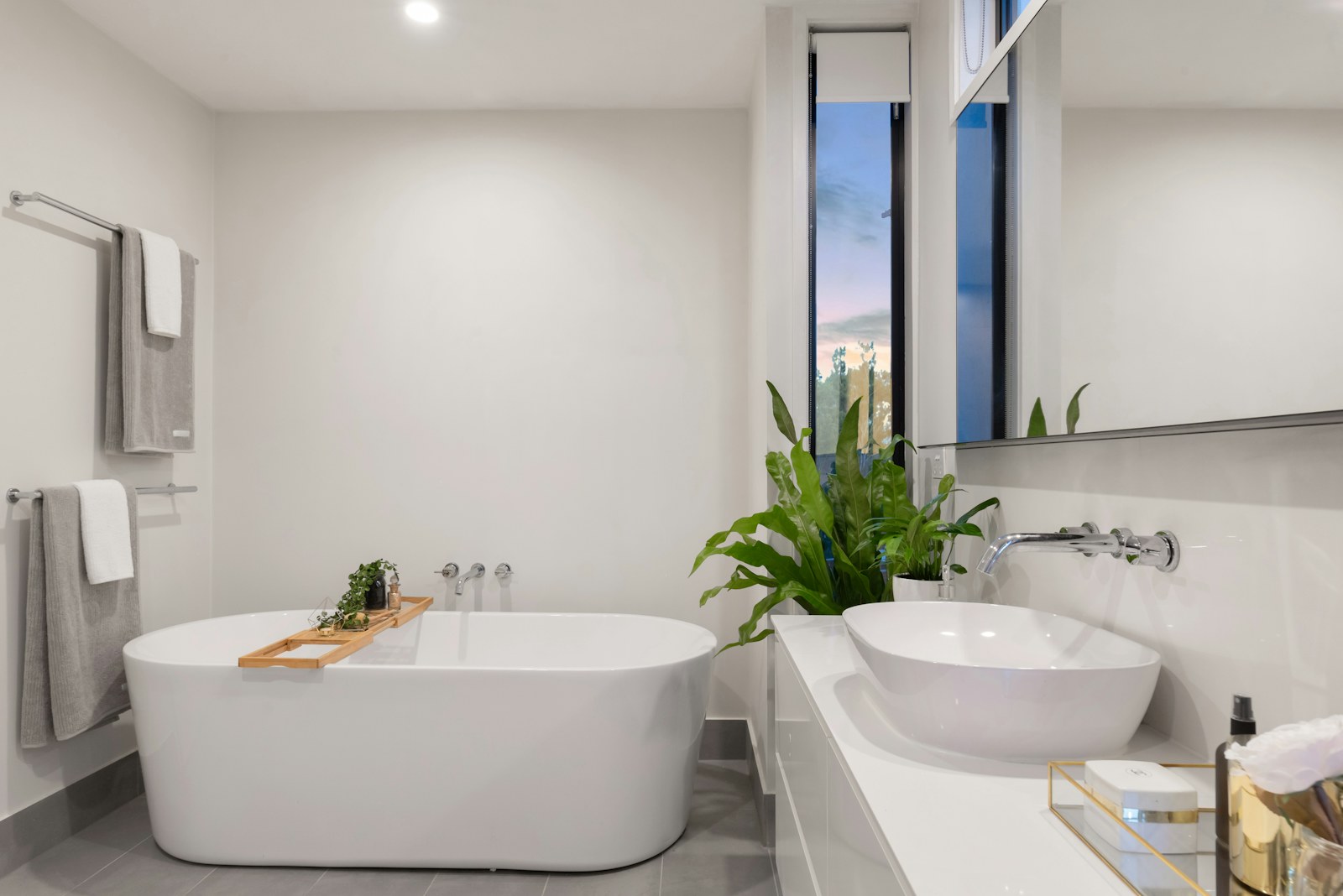 White bathtub and basin with grey towels on rails beside a tall window