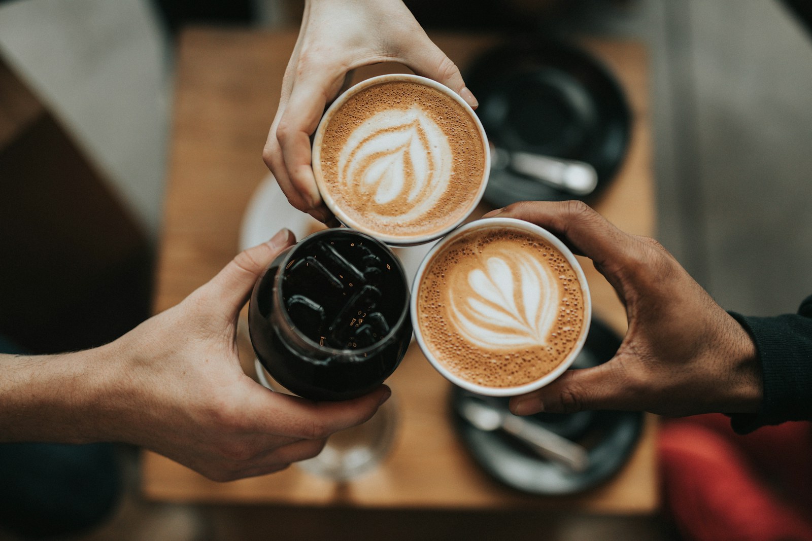 Hands holding three cups of coffee with latte art
